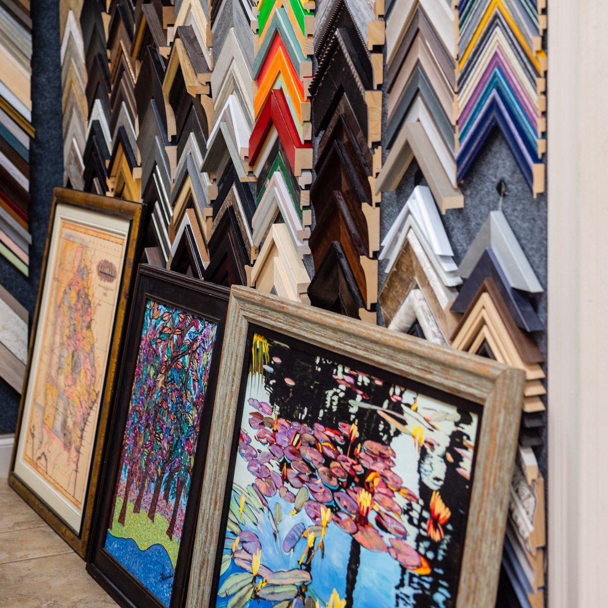 Framed colorful artwork leaning in a shop with rows of picture frames behind it