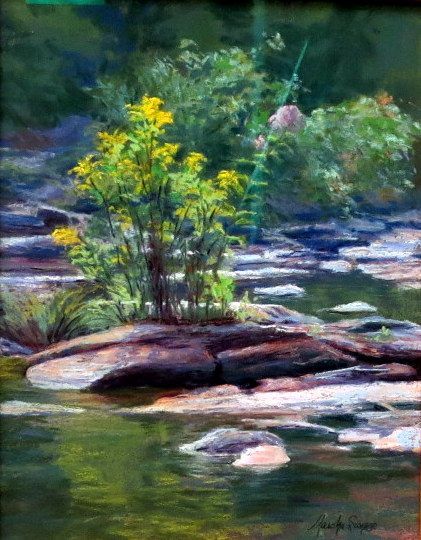 A small flowering shrub grows on a rocky stream bank with green water and blurred forest in the background.