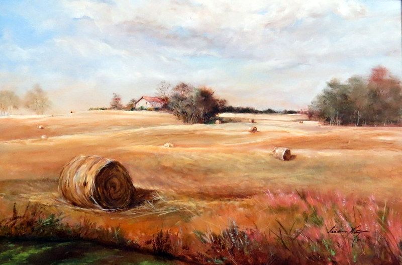 Hay bales in a golden field with trees and a cloudy sky at sunset