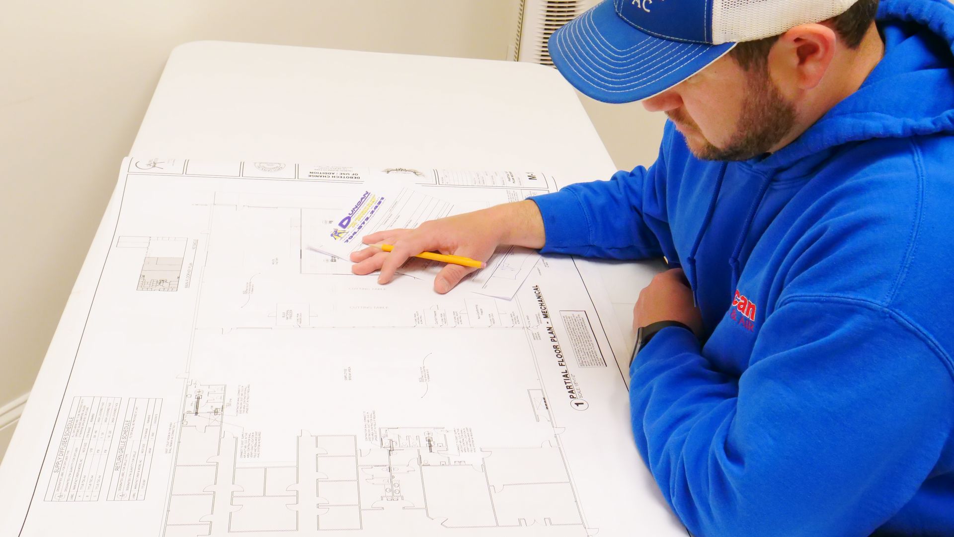 A man is sitting at a table looking at a blueprint.
