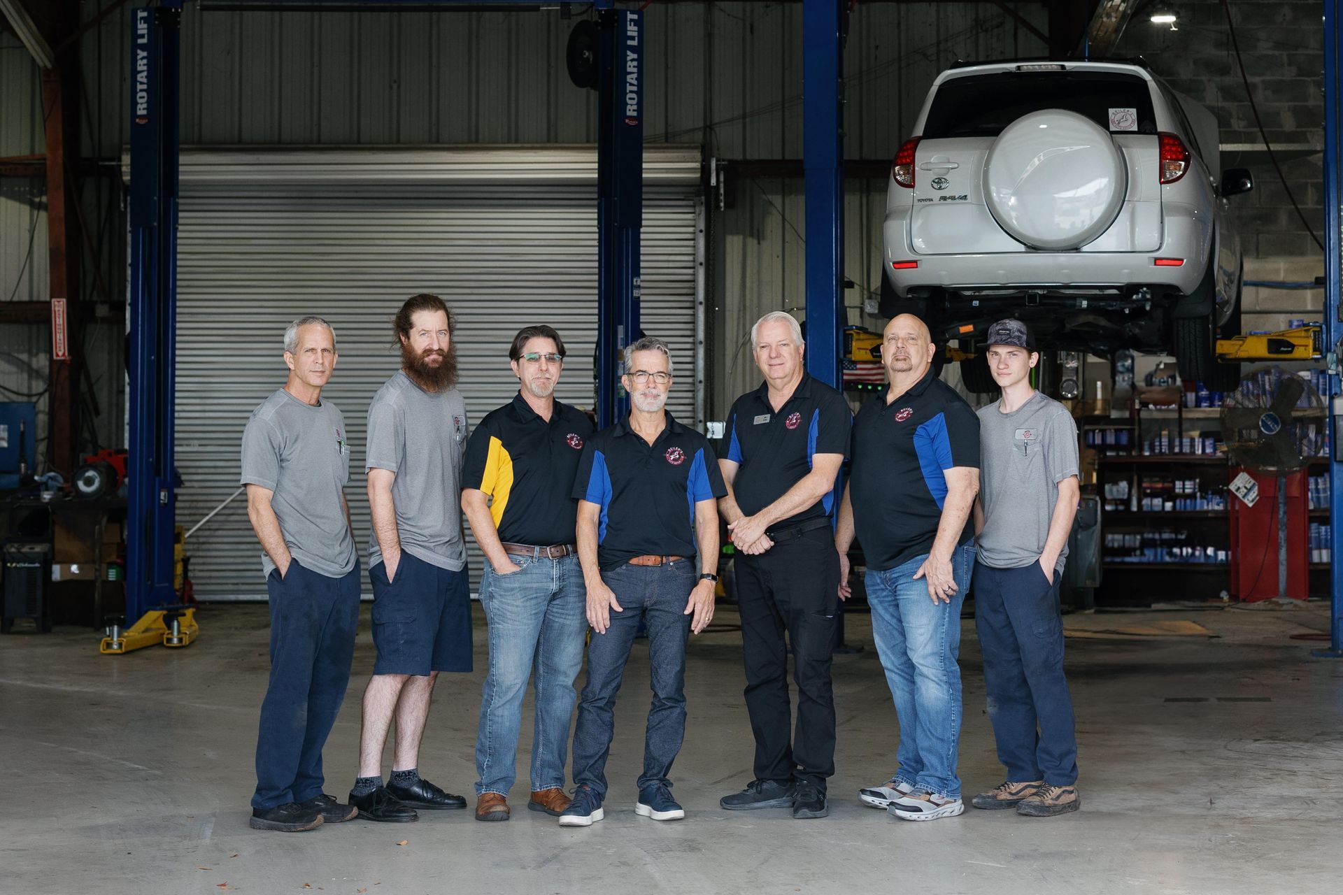 mechanics standing in a garage with a lifted SUV on a lift behind them.