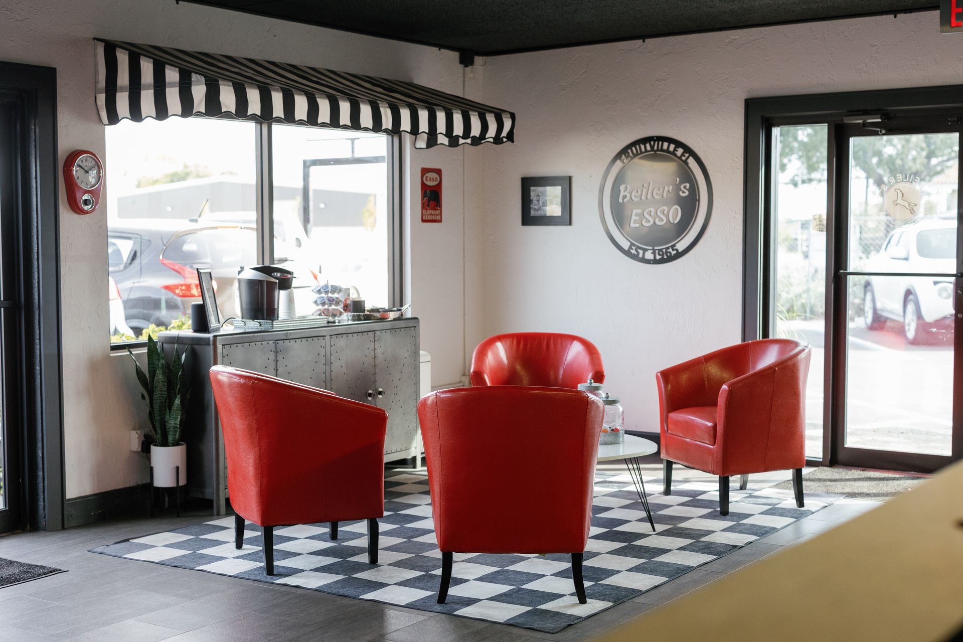 Four red chairs around a small table on a geometric rug in a waiting area with a striped awning.