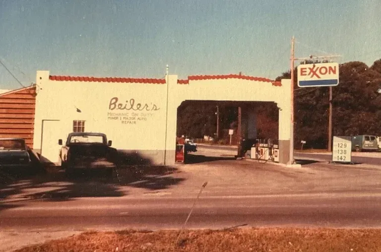 Old roadside Exxon gas station with a vintage car parked outside and a white building in warm sunlight