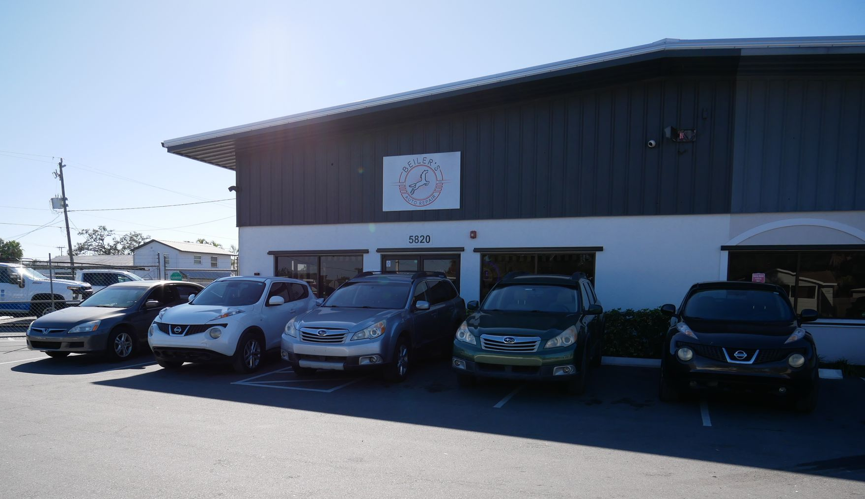 Cars parked in front of a building with a logo, sunny outdoor setting.
