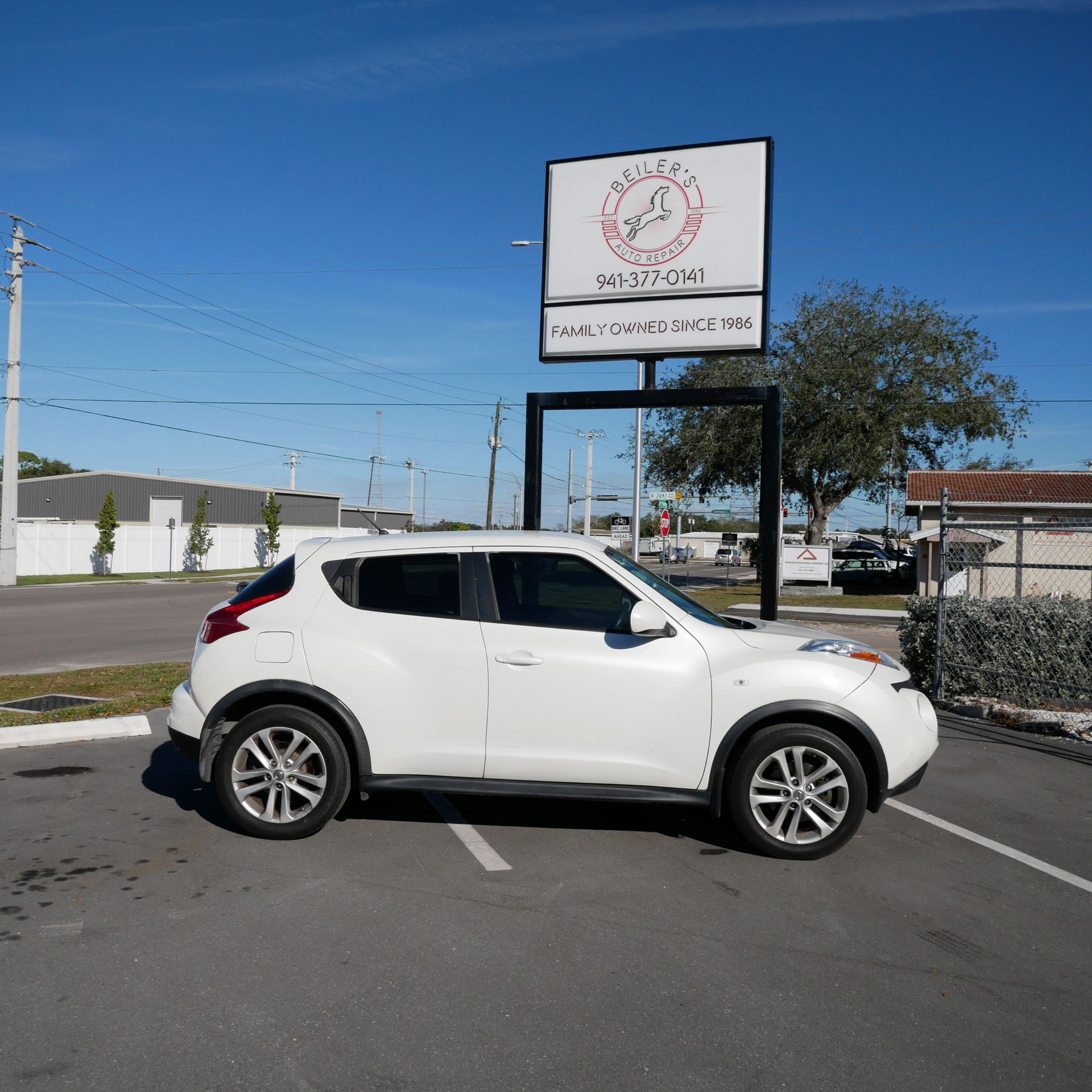 White Nissan Juke parked in front of a business sign on a sunny day.