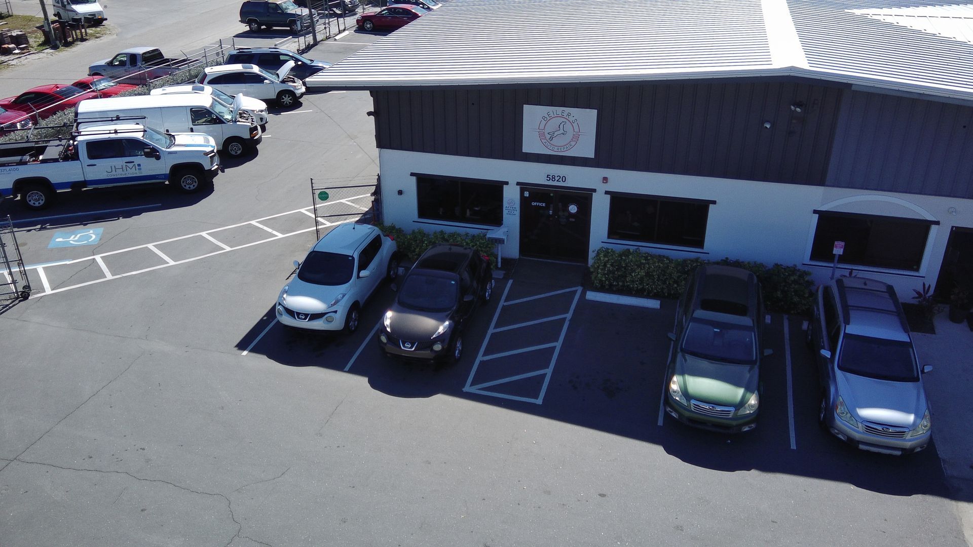 Cars parked outside a commercial building on a sunny day. A variety of vehicles are present.