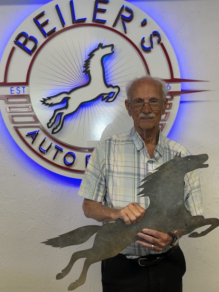 Man holding a horse silhouette, standing in front of Beiler's Auto, with a sign featuring a horse.