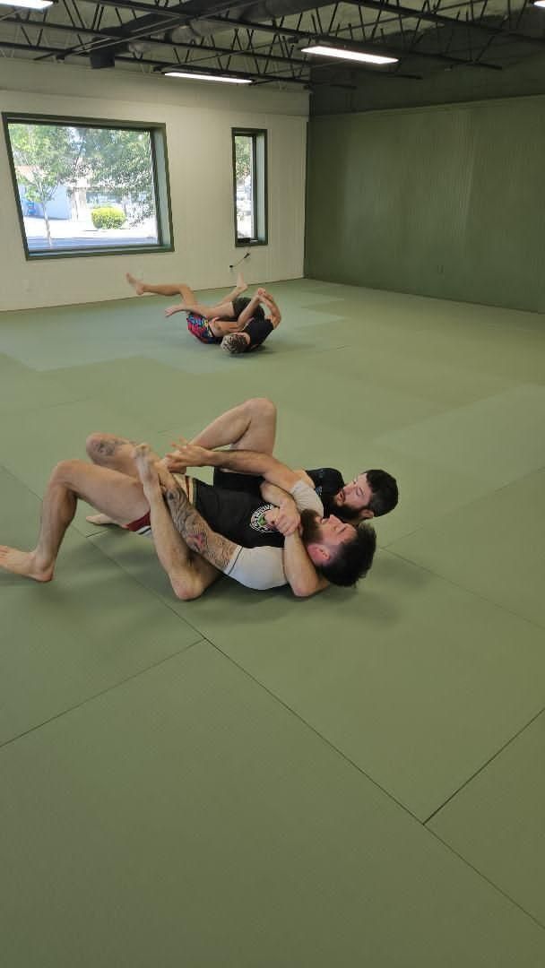 Two grapplers in gis on a mat as a standing athlete controls a grounded opponent by the legs