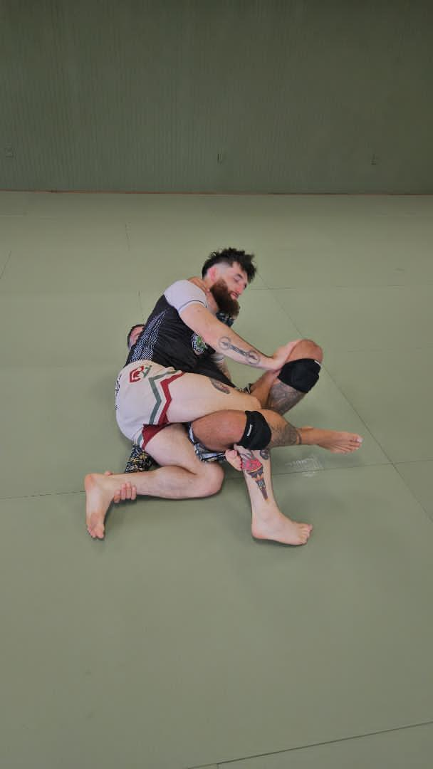 People practicing grappling drills on a mat in a martial arts gym
