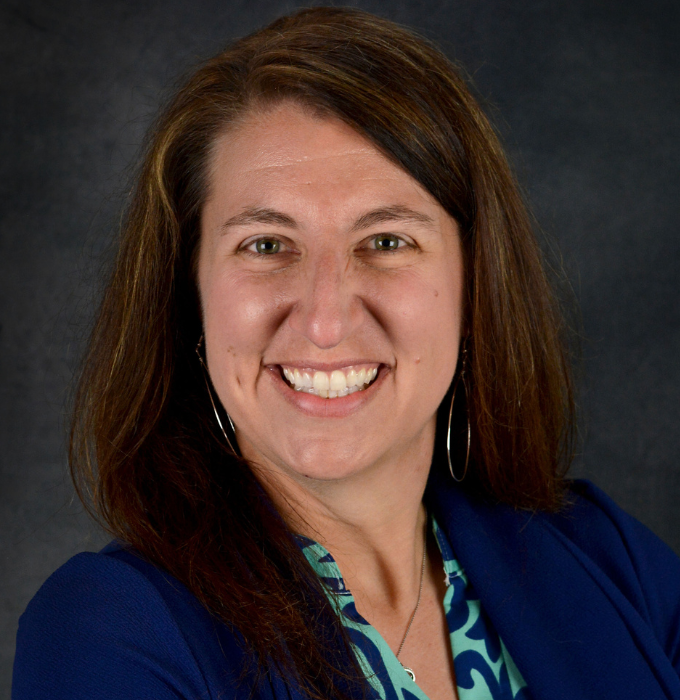 A woman wearing a blue jacket and a blue shirt is smiling for the camera.
