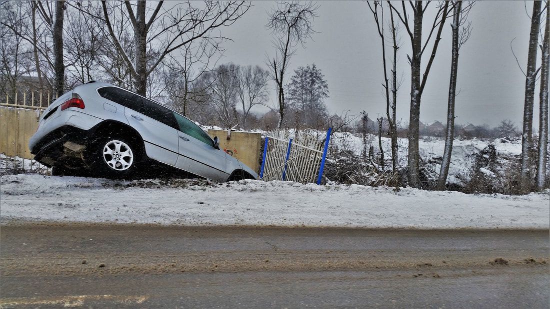 Picture of a white car crashed in the snow on the side of the road requiring roadside assistance.