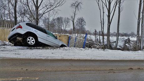 Picture of a white car crashed in the snow on the side of the road requiring roadside assistance.