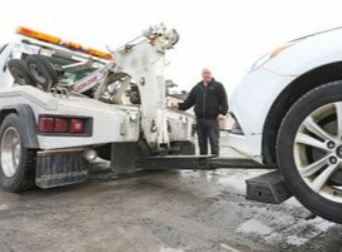 Picture of a service man operating the wheel lift mechanism on the tow truck. The tow truck is hoisting up a blue car.