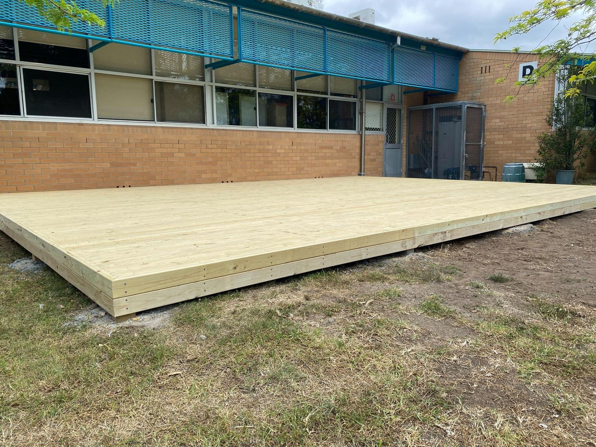 A newly constructed, light-colored wooden deck against a brick building with a blue awning.