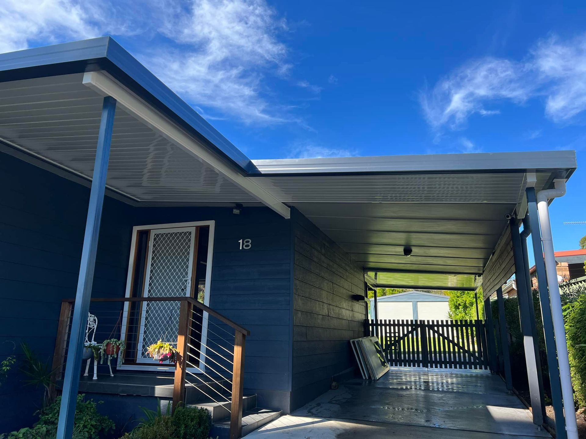 Blue house with carport; gray roof, white trim, and blue sky.