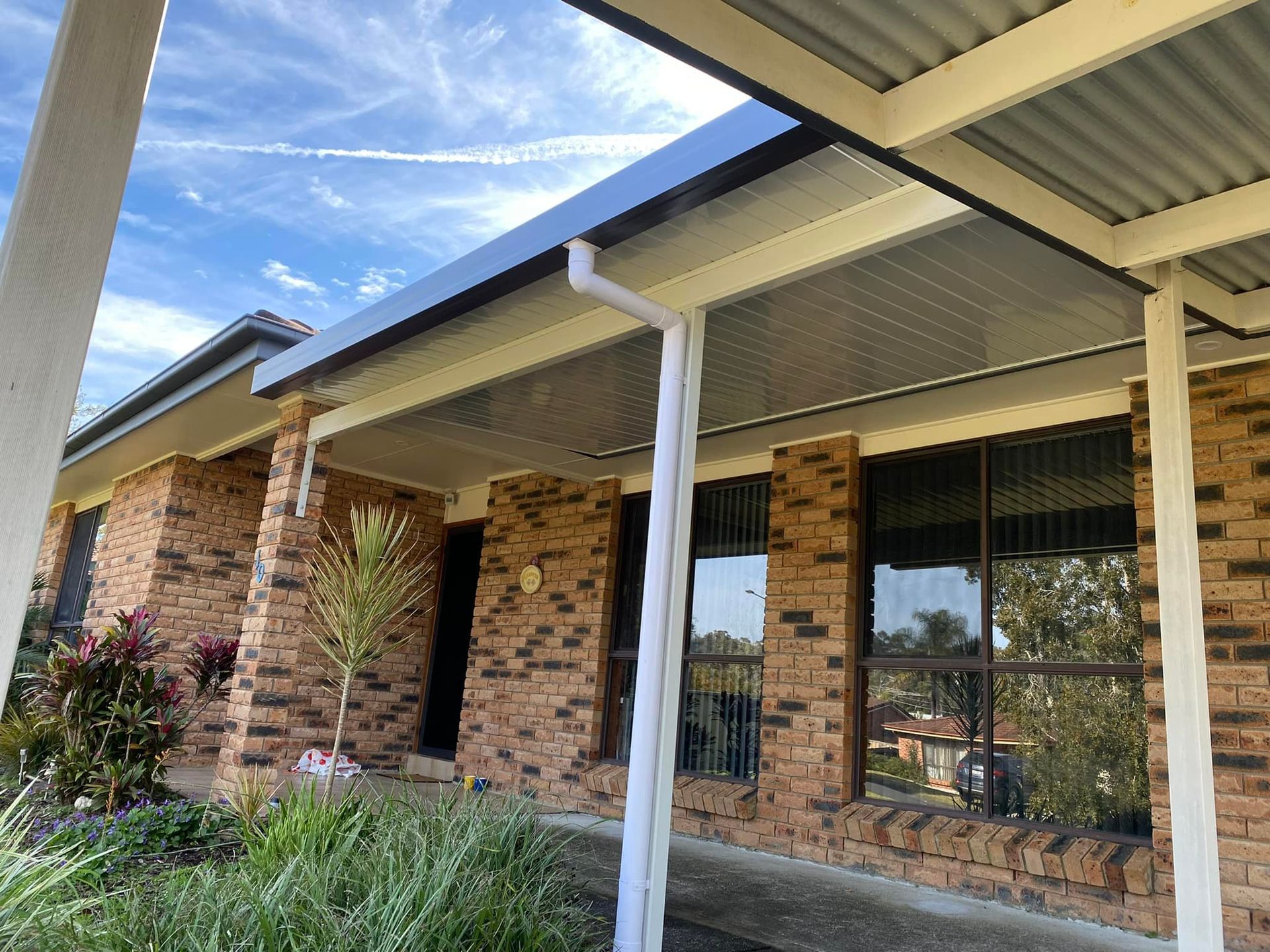 A brick house with a covered walkway. The roof is corrugated metal. Blue sky in the background.