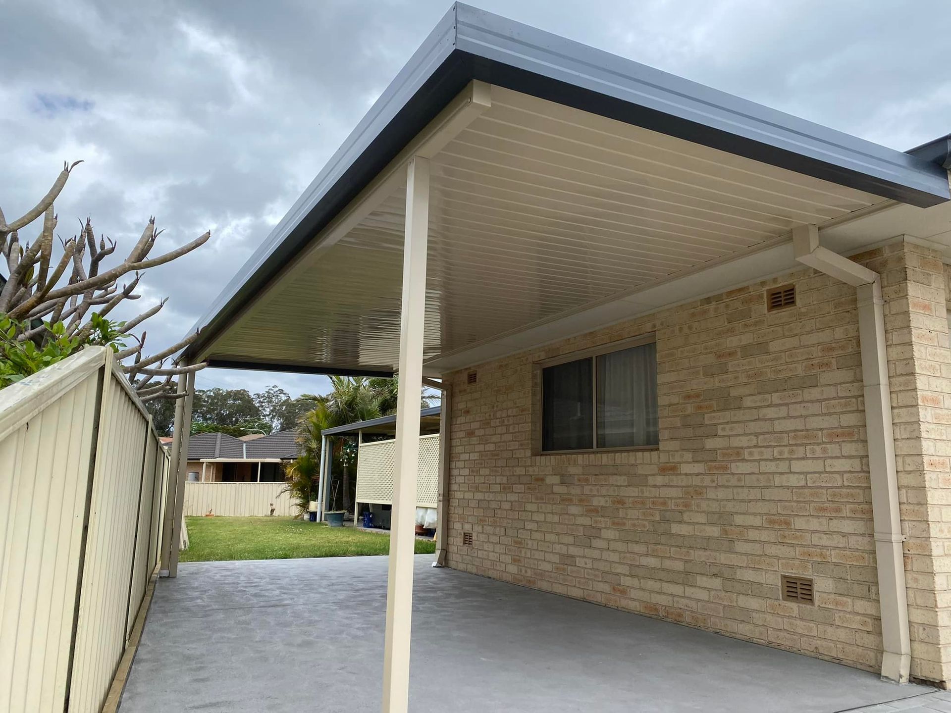 Carport with light beige brick wall, light gray roof, and concrete driveway.