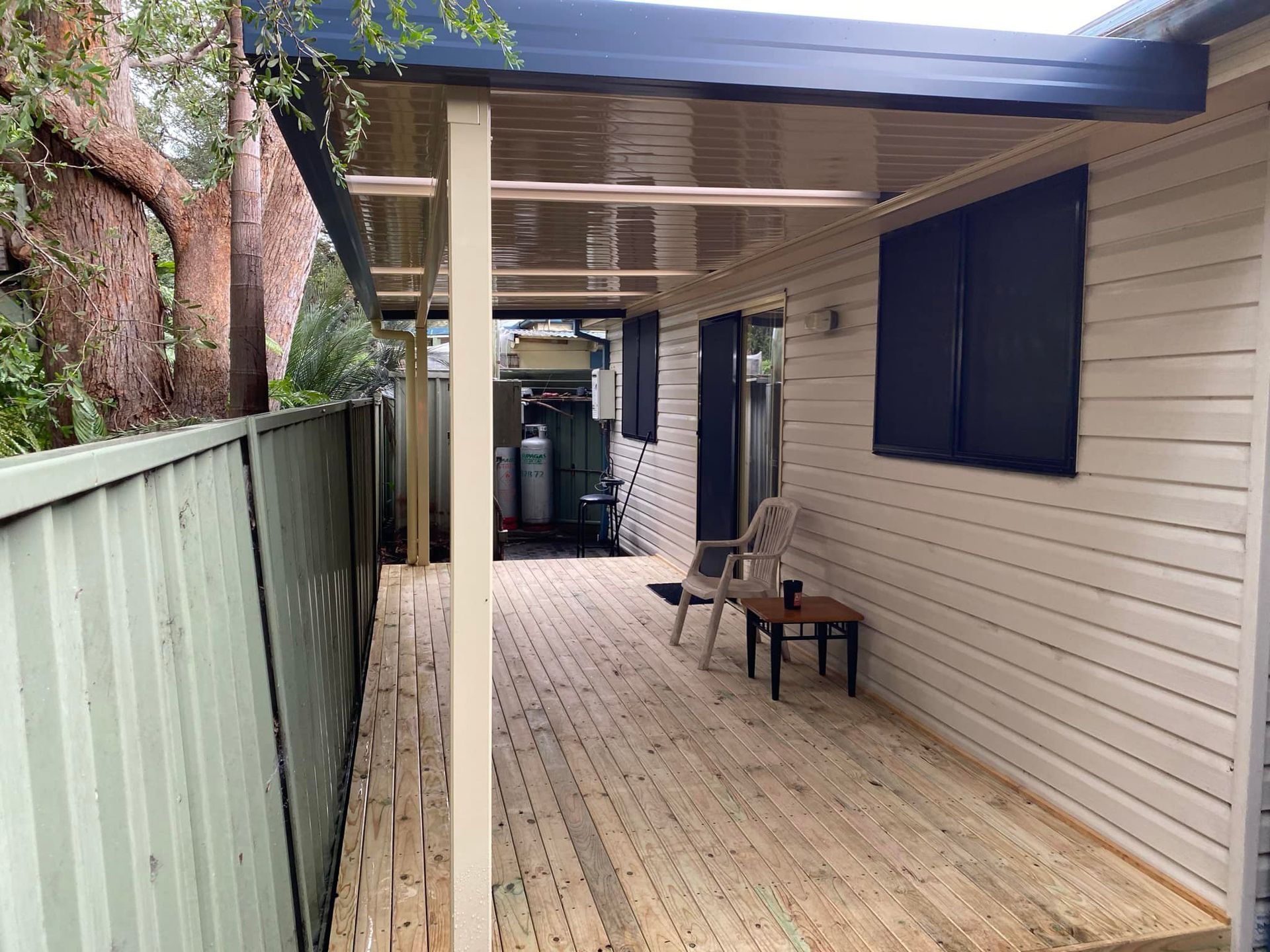 Covered wooden deck with fence, siding, chair, and table.