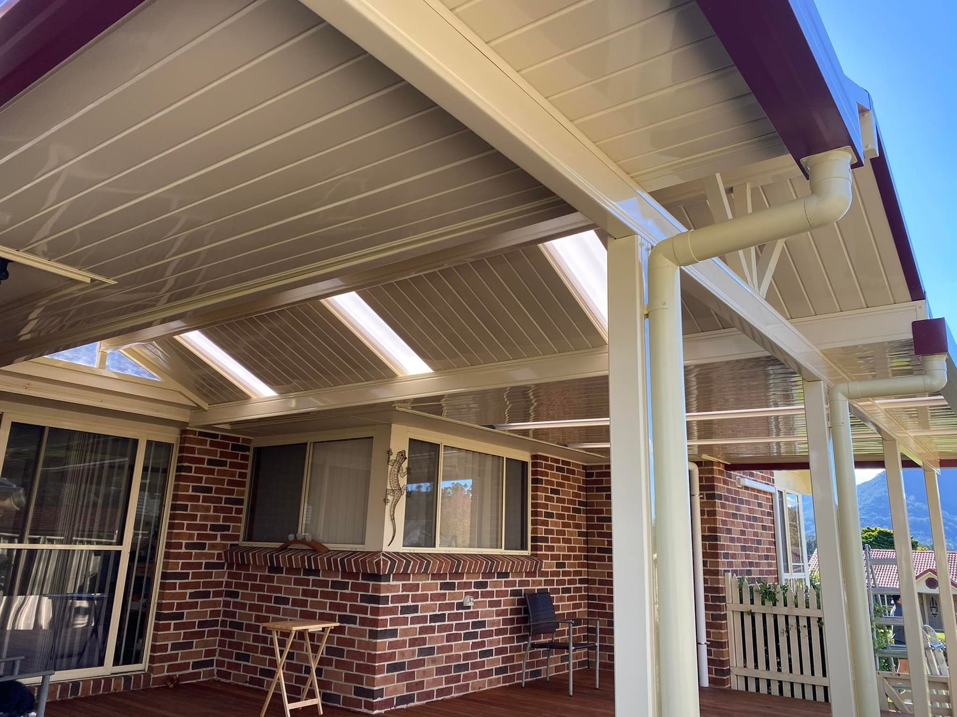 Wooden pergola over a patio with grass and trees in the background on a sunny day.