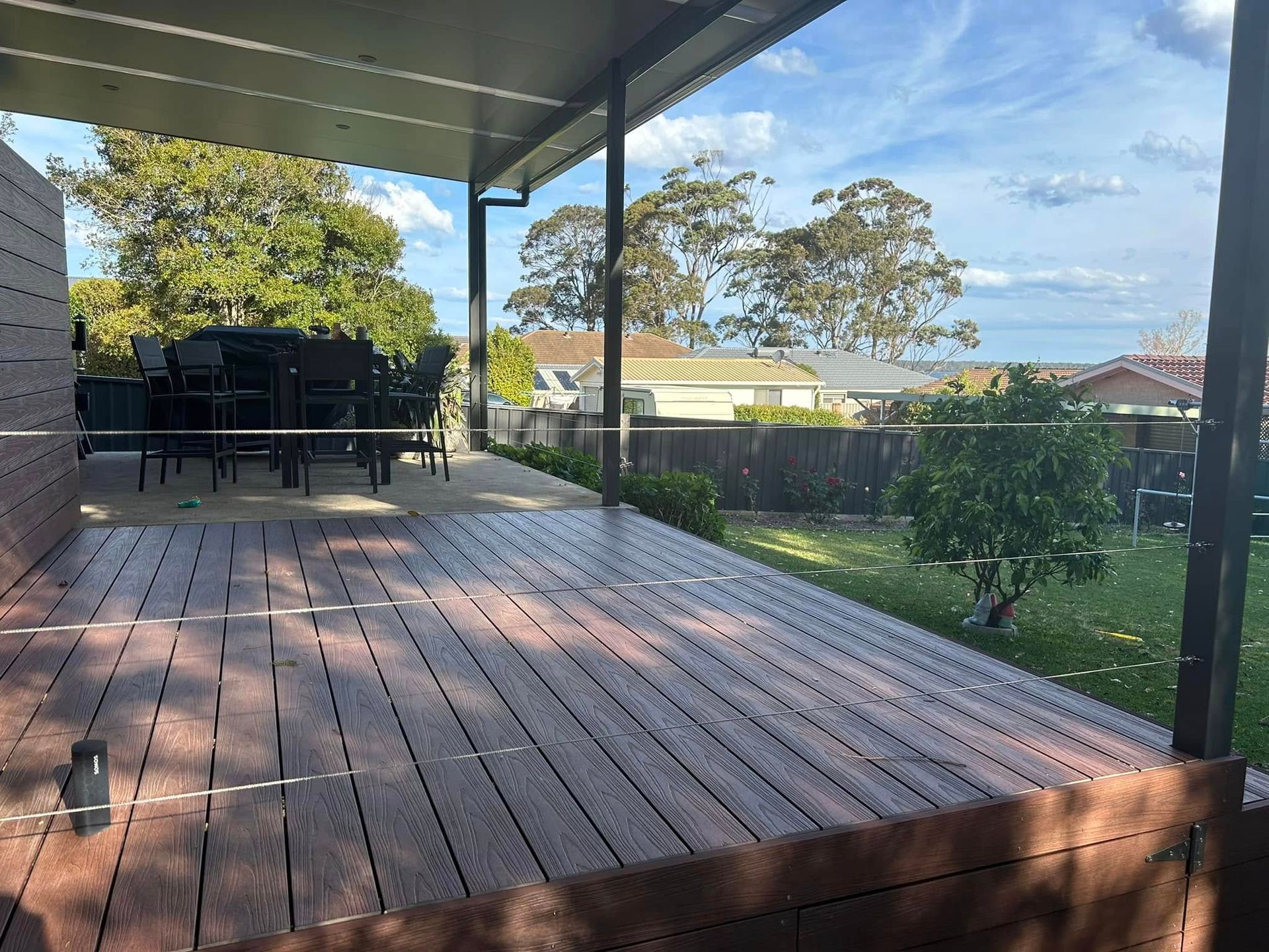 Wooden deck with glass railing, covered patio, overlooking a backyard with trees and houses.