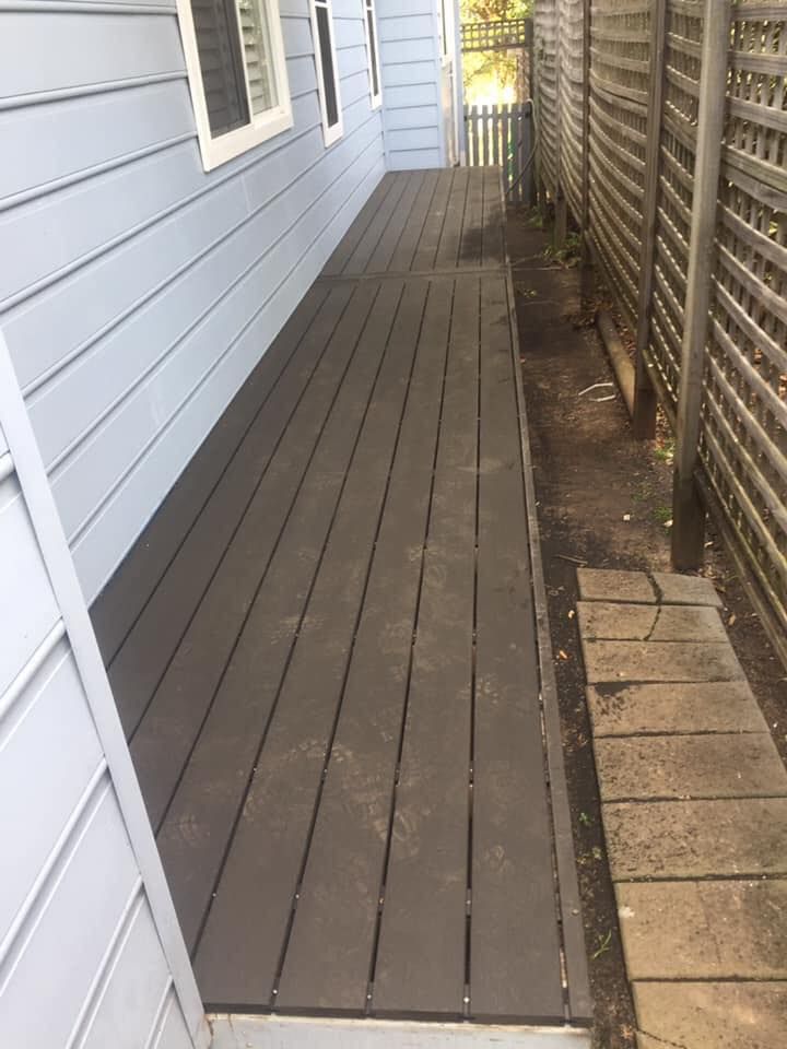 A wooden deck next to a house with a fence.