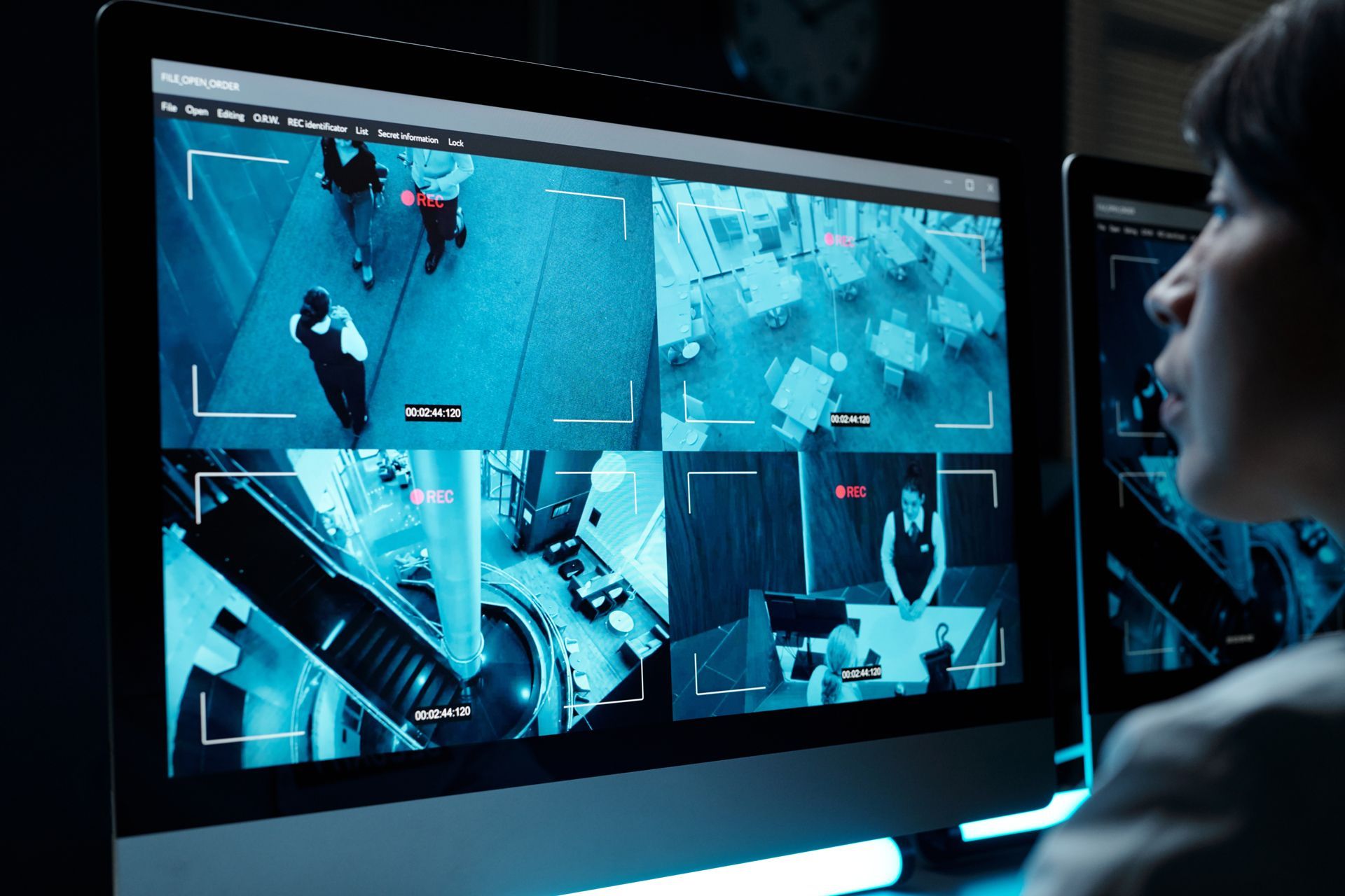 A woman is sitting in front of a computer monitor looking at security cameras.