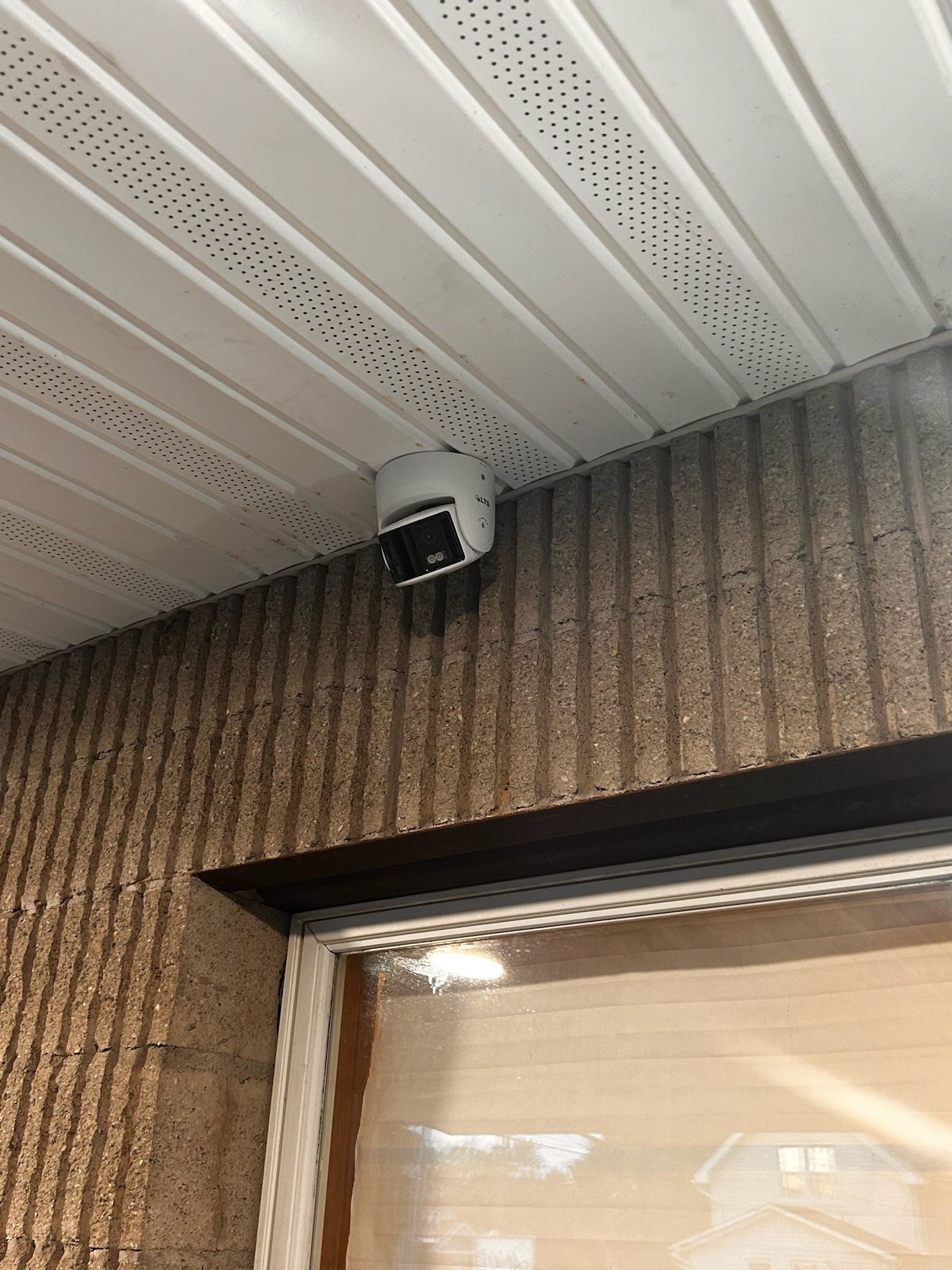 Security camera mounted on a ceiling of a building with white and brown siding.