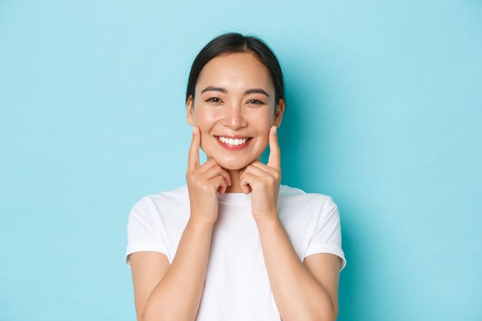 a woman in a white shirt is smiling and touching her face