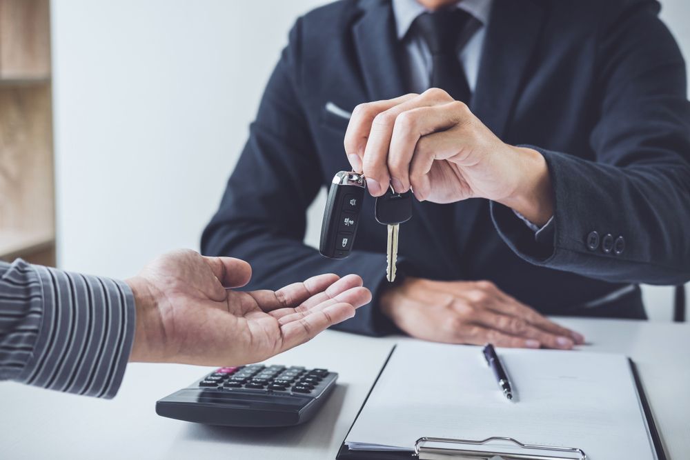 A Man in a Suit is Handing a Car Key to Another Man — Rauseo Group in Zuccoli, NT