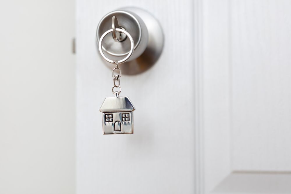 House Shaped Keychain Hanging from A Silver Doorknob on A White Door — Rauseo Group in Zuccoli, NT