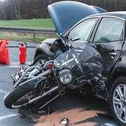A motorcycle has crashed into a car on the side of the road.