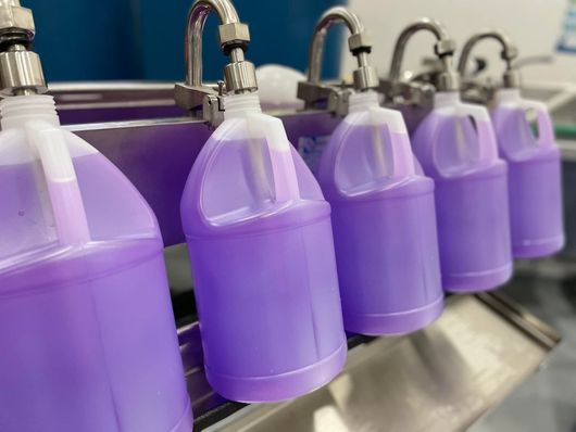 Botellas moradas en una cinta transportadora siendo llenadas en una fábrica.