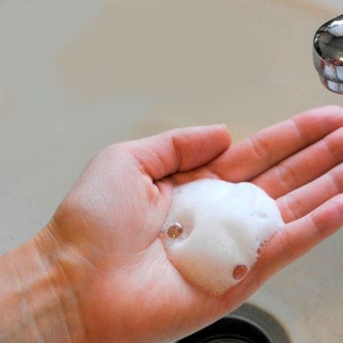 Mano sosteniendo una burbuja de jabón espumosa bajo el agua corriente de un lavabo.