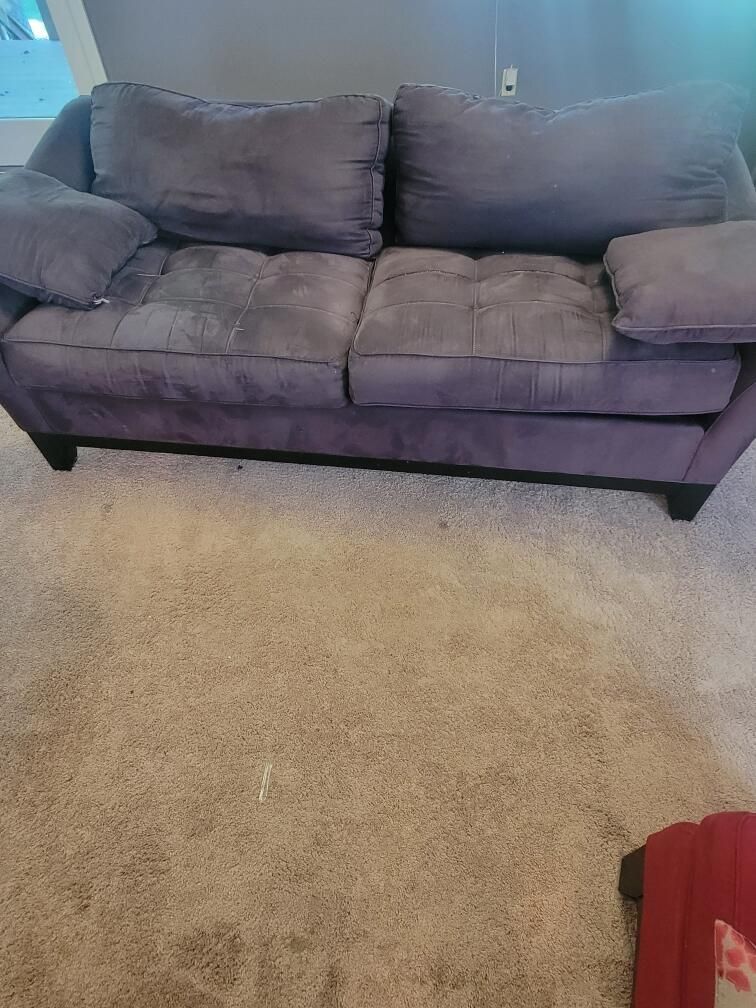 A purple couch is sitting on a carpet in a living room.