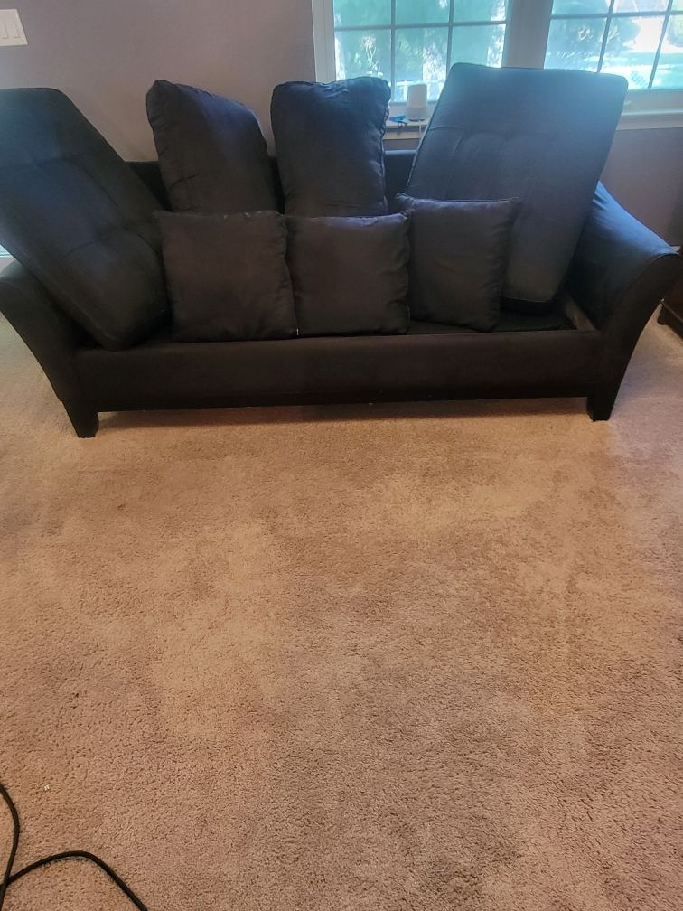 A black couch is sitting on top of a carpeted floor in a living room.