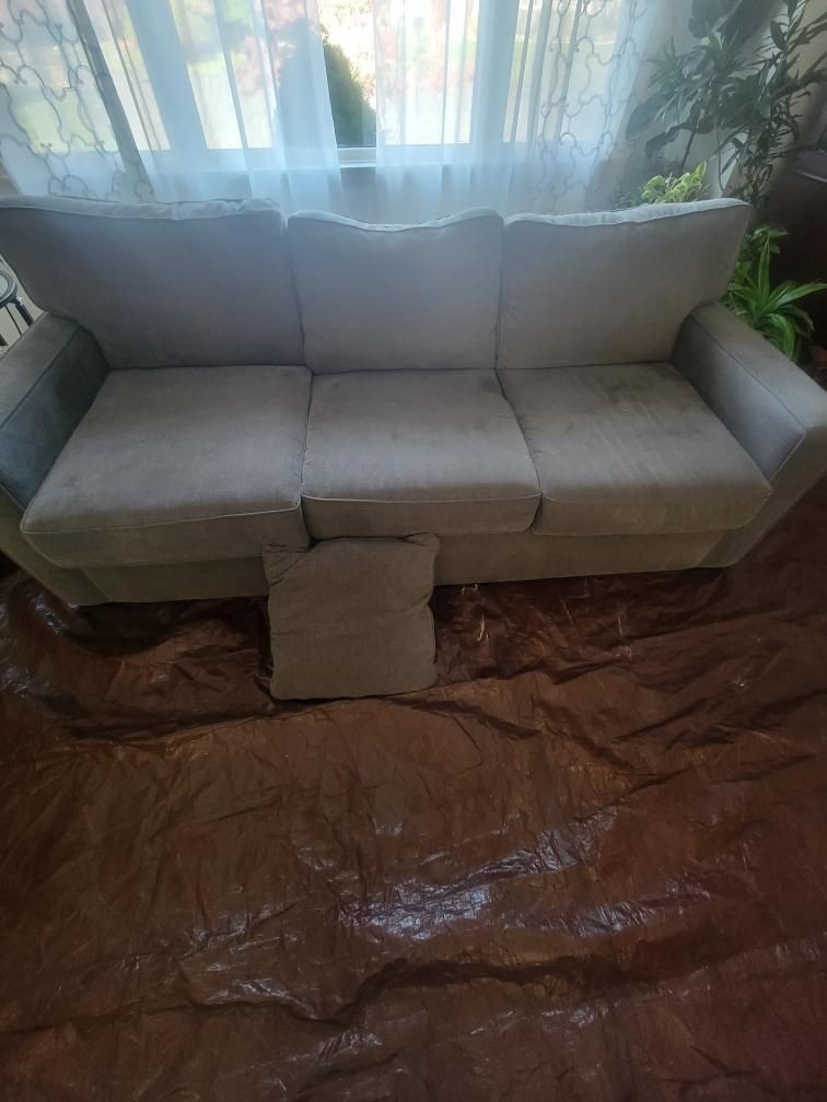 A white couch is sitting on top of a brown tarp in a living room.