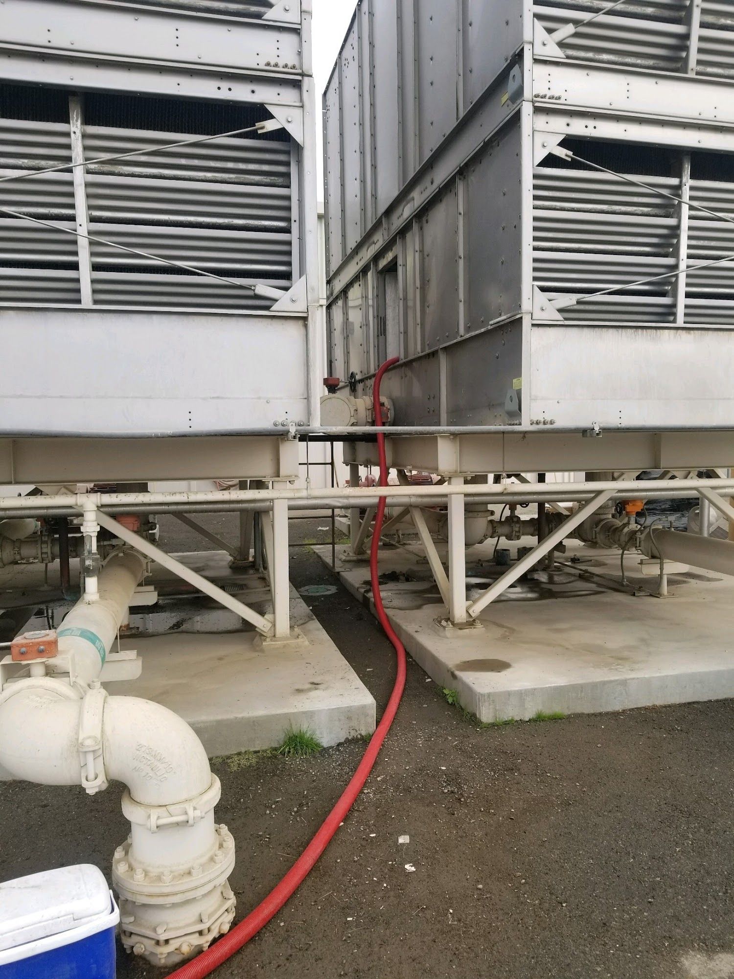 Industrial cooling equipment with red hose on gravel ground beside metal platforms and pipes