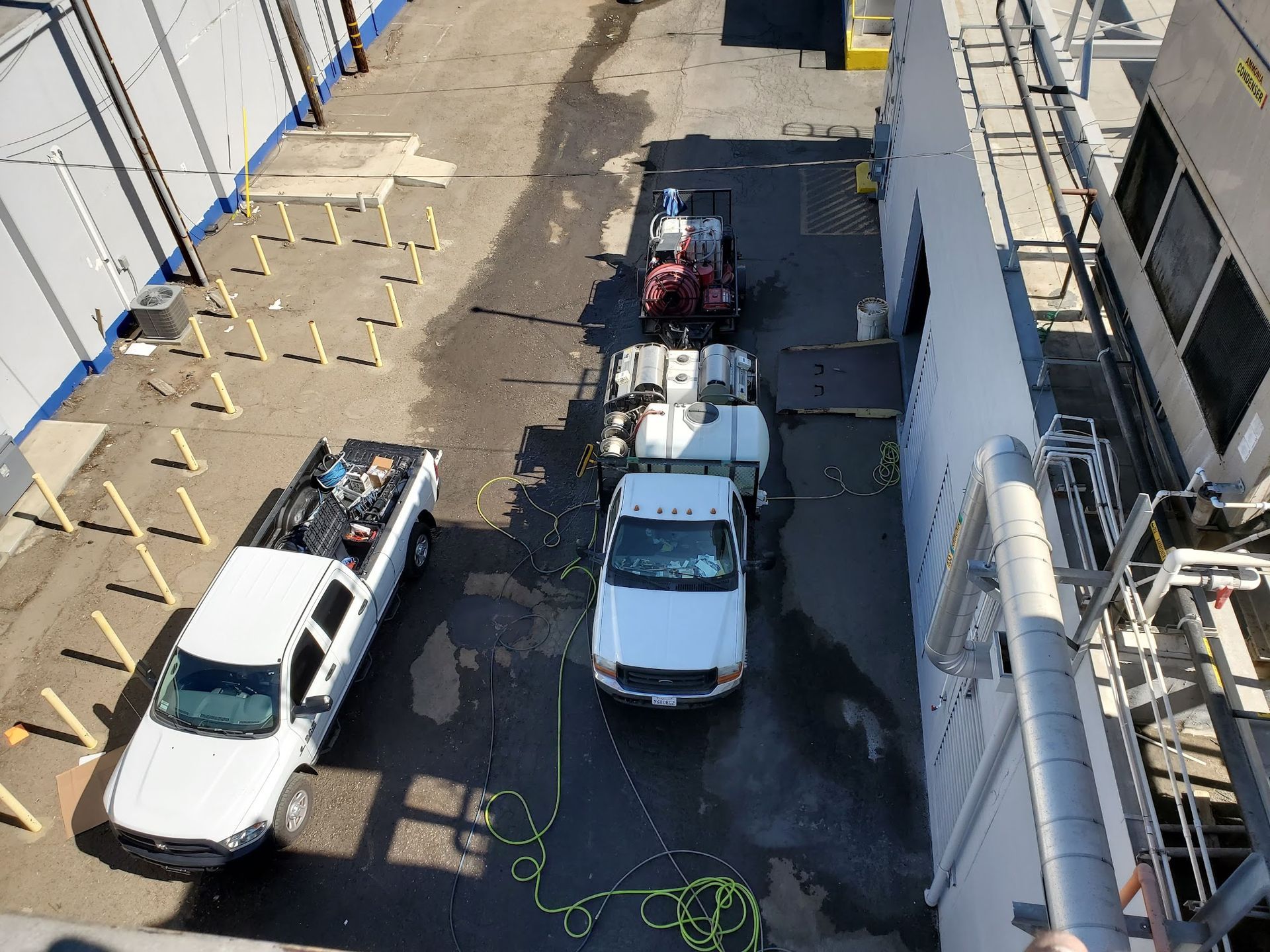 Overhead view of a narrow alley with parked white trucks, a van, and construction materials along the walls