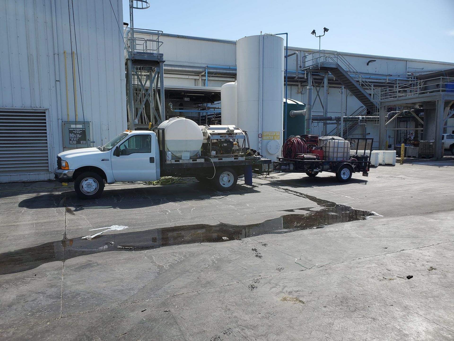 White utility truck and red pickup parked by an industrial warehouse loading area