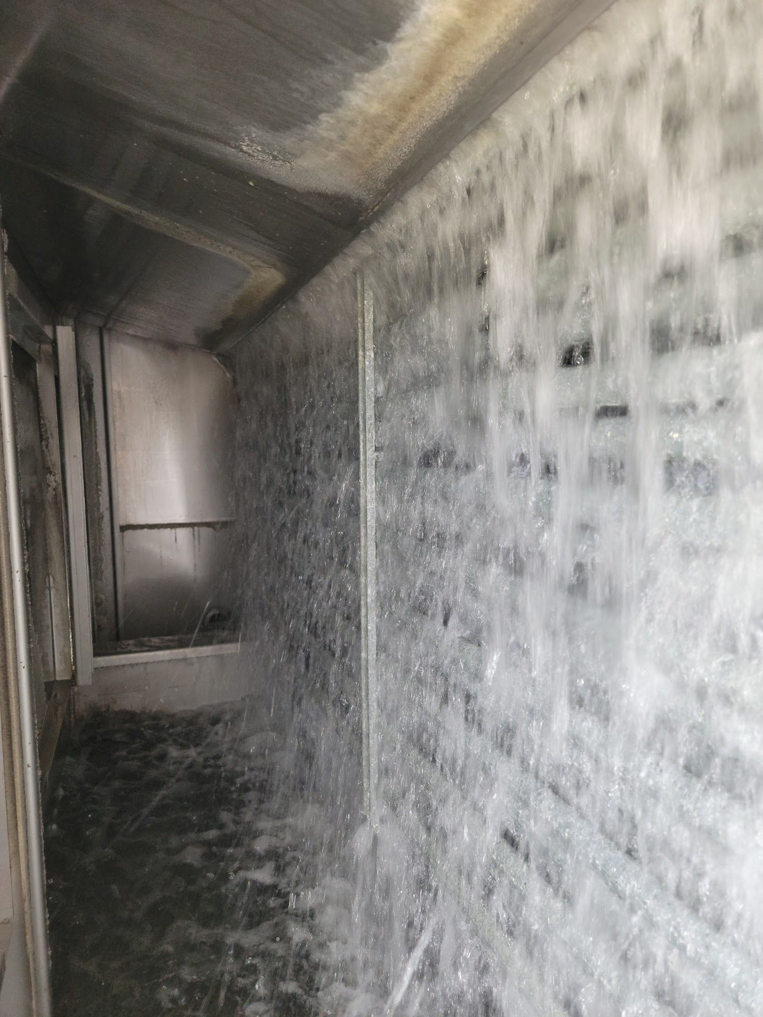Narrow industrial corridor with water cascading down a wall and pooling on the floor