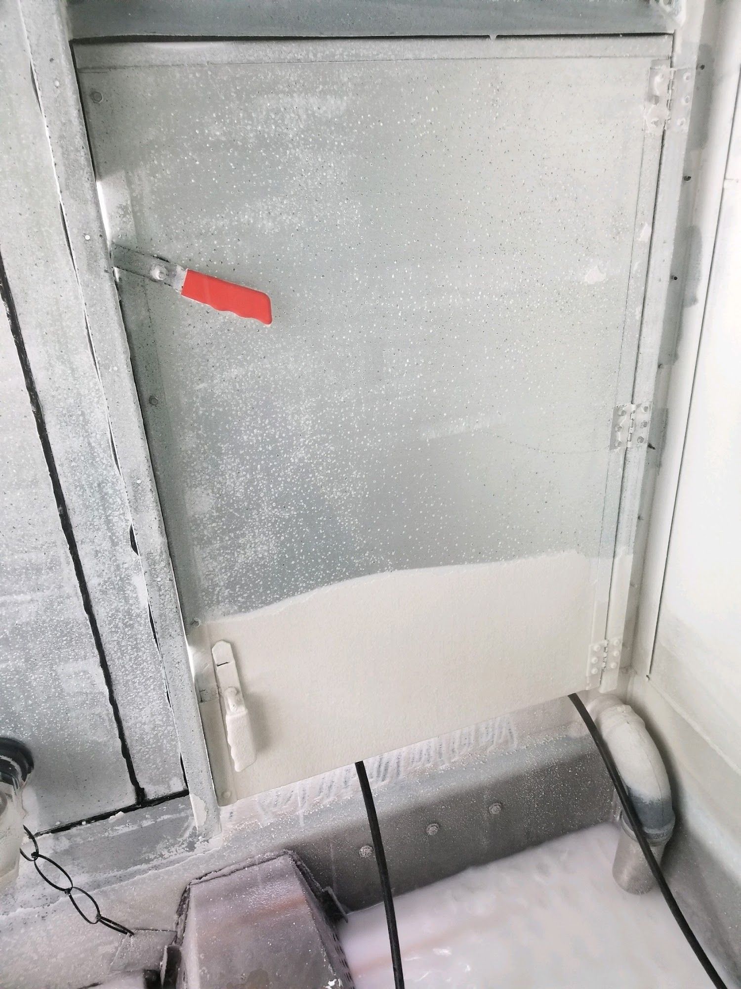 Metal door or panel with a red handle and a light gray lower section, seen in a utility area.