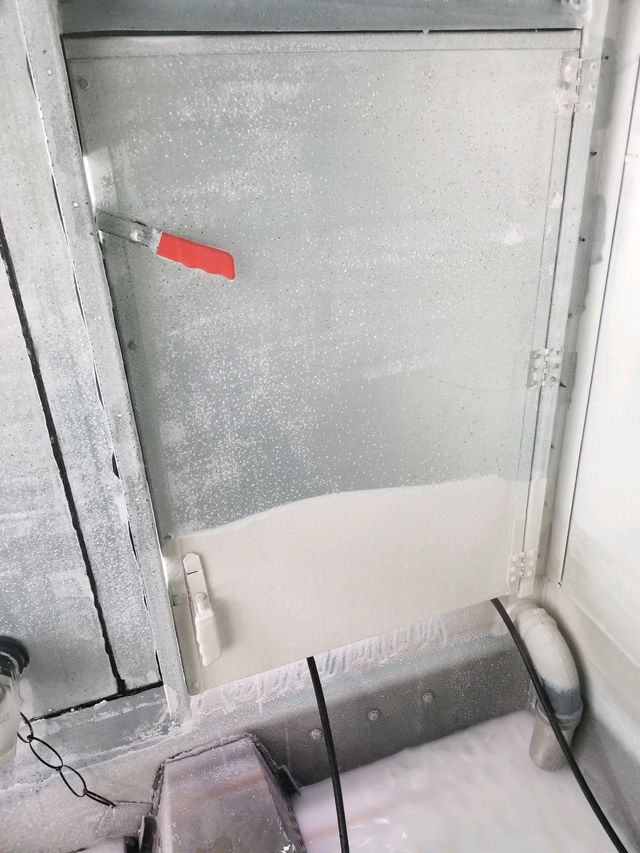 Metal hatch or window with frosted glass and a red handle in a gray industrial setting
