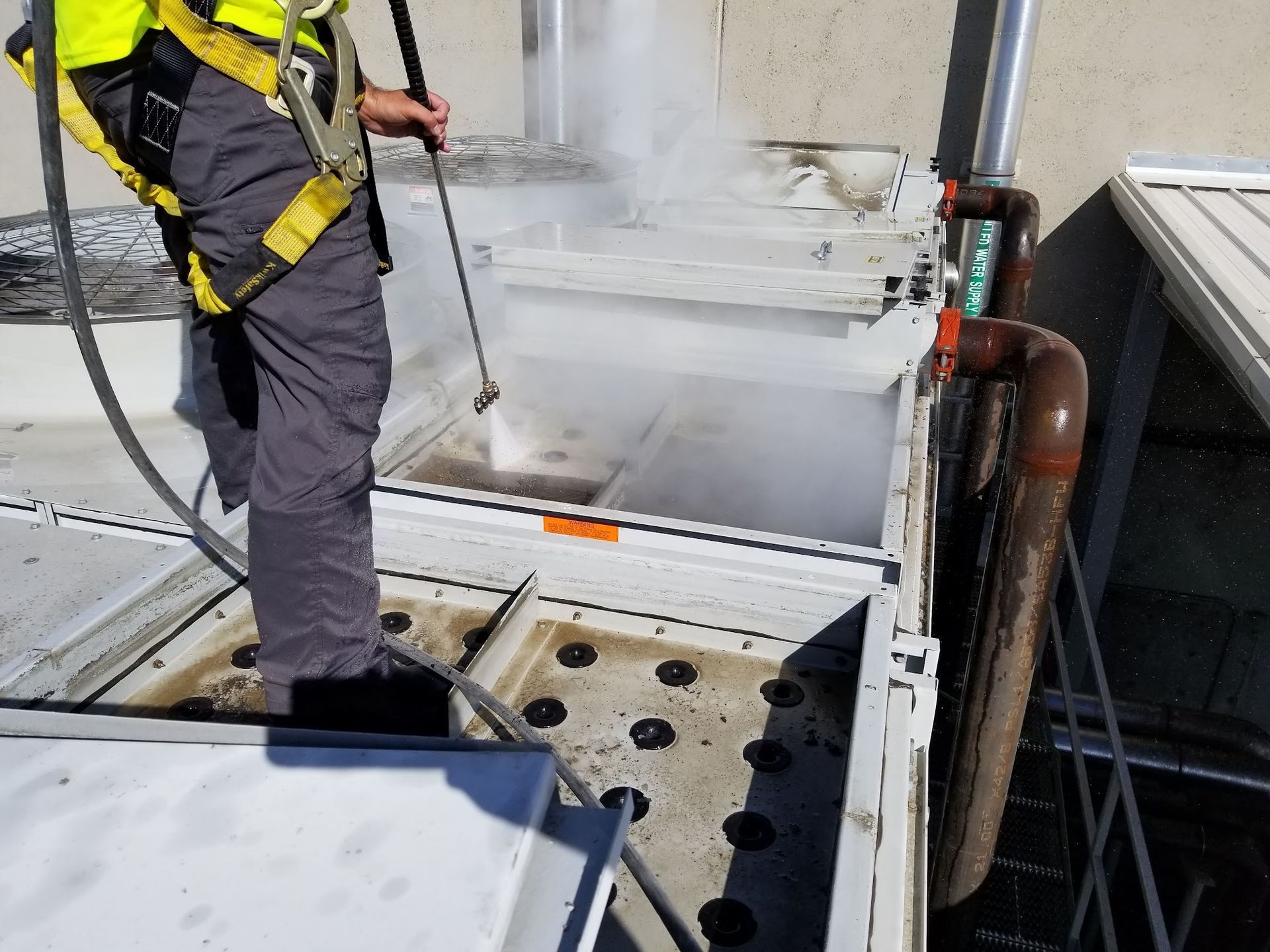 Worker in yellow safety harness inspecting a white industrial tank on a metal platform