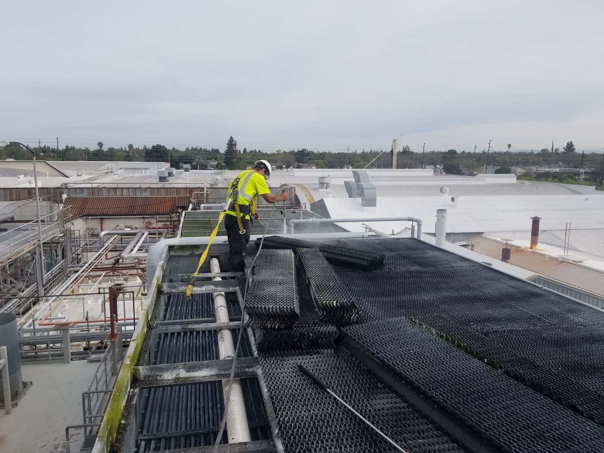 Worker in neon safety gear spraying black roofing material on a construction site