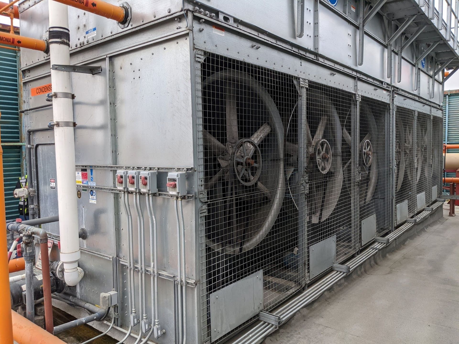 Industrial HVAC unit with large cooling fans and metal piping along a building exterior