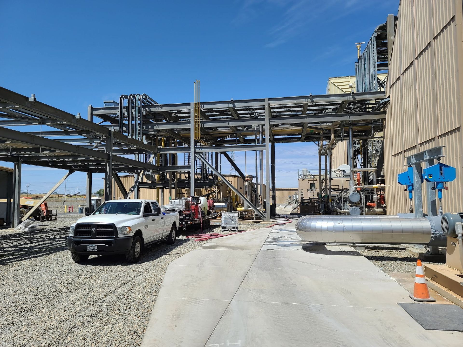 Industrial site with pipes, scaffolding, a white truck, and workers under a clear blue sky