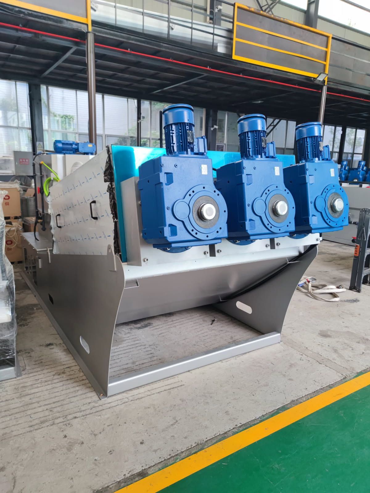 Industrial mixer machine with three blue motor housings in a factory workshop