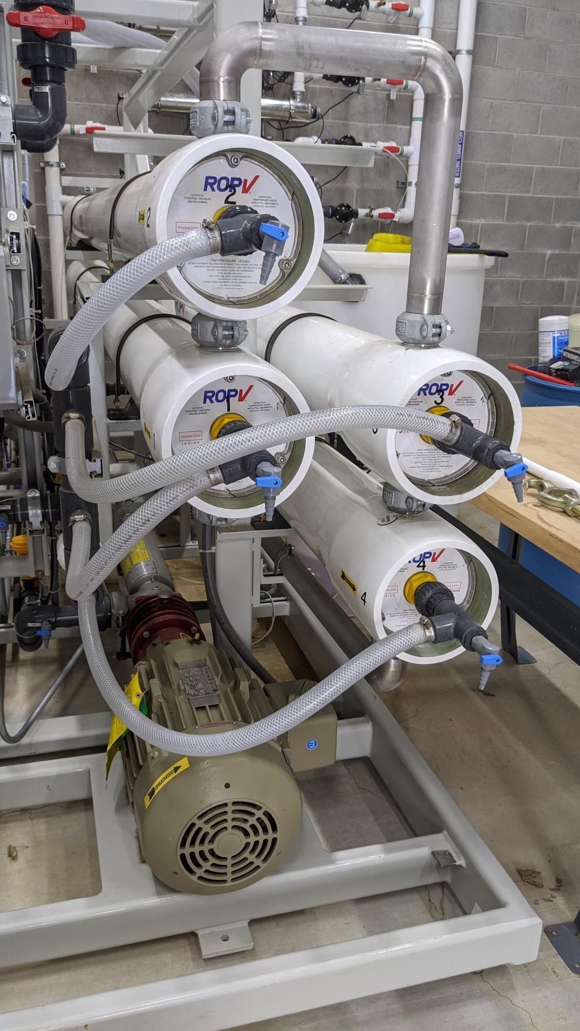 Industrial filtration system with white cylindrical units, clear tubing, and valves in a metal frame