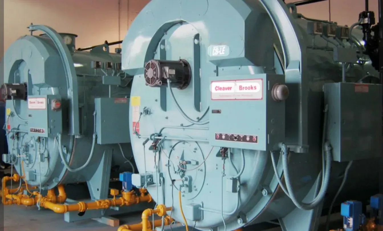 Large blue industrial boiler units with pipes and valves in a factory room