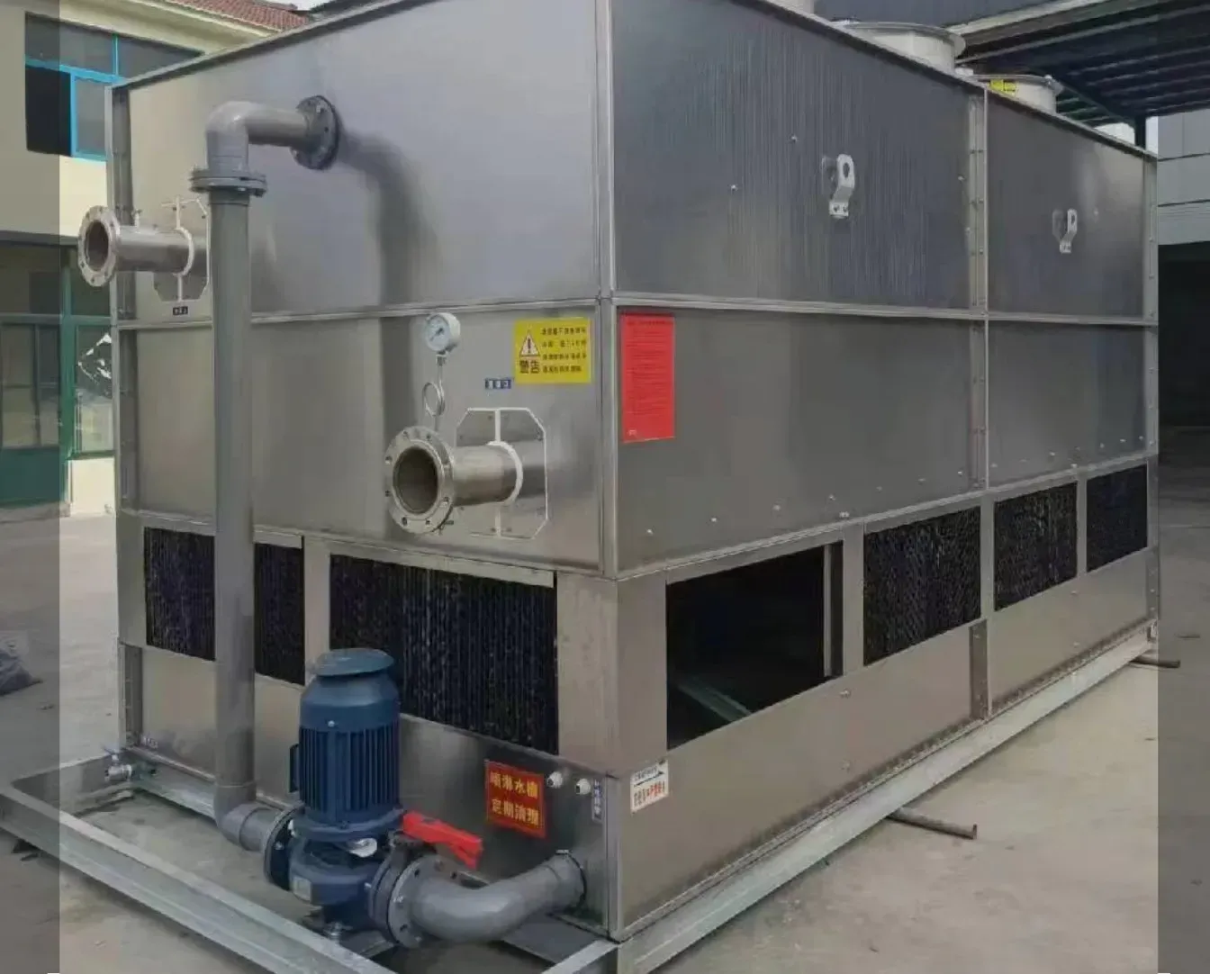 Industrial water chiller unit with pipes, fan grilles, and a motor on a concrete pad outdoors